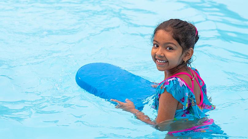 Girl swimming in an outdoor pool using a blue flutter board