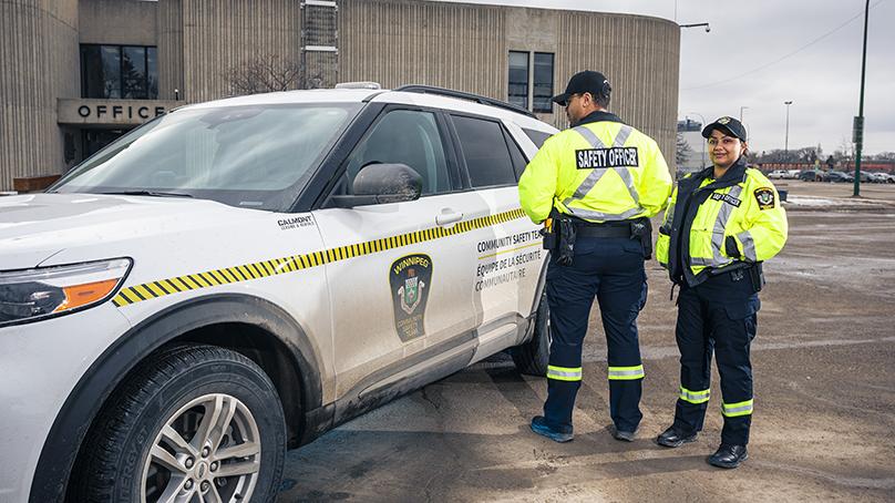 Two community safety officers wearing high visibility jackets standing in front of a patrol vehicle