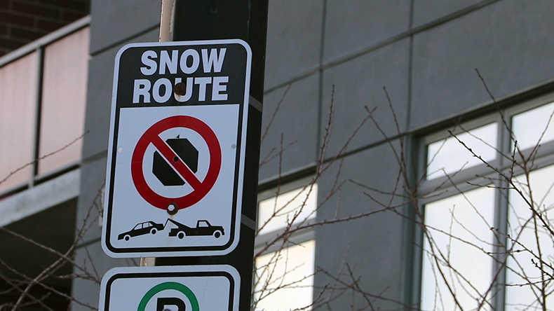 A No Parking - Snow Route sign is displayed outside a building in the winter time. 