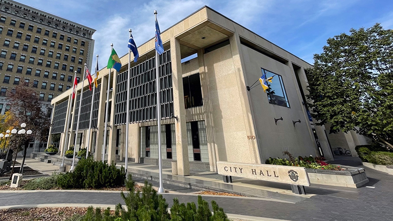 City Hall Council Building showing flags with blue sky, trees, and greenery.
