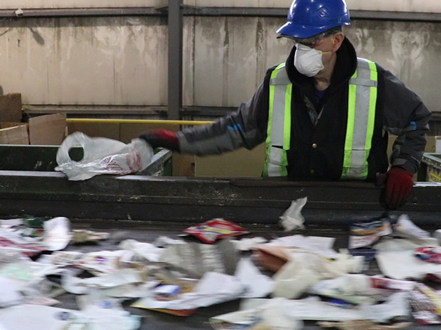 Employee removing plastic bags from sorting line by hand at recycling facility