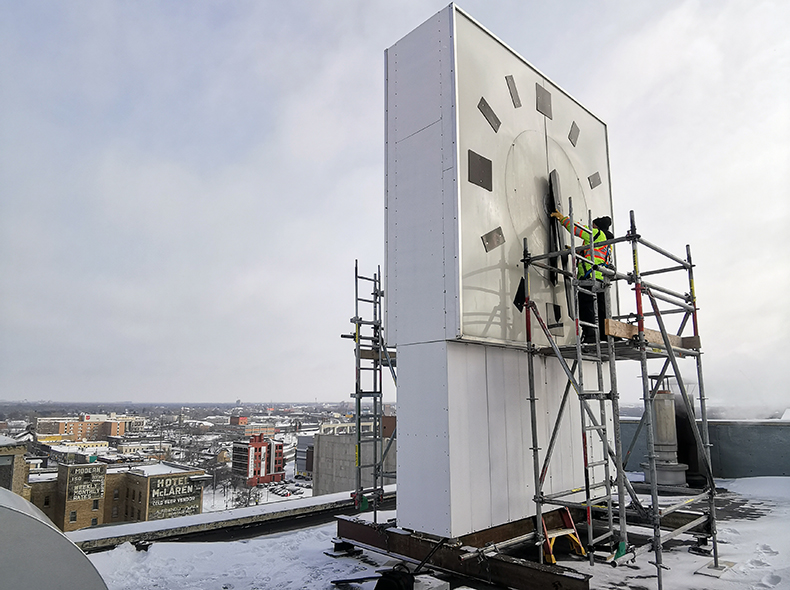 A worker in a safety vest changes the time of the large clock atop Winnipeg's City Hall