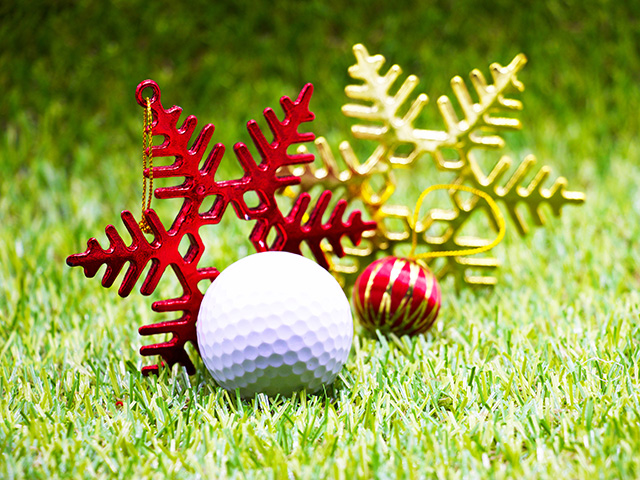 golf ball on the green with red and gold Christmas tree ornaments behind it