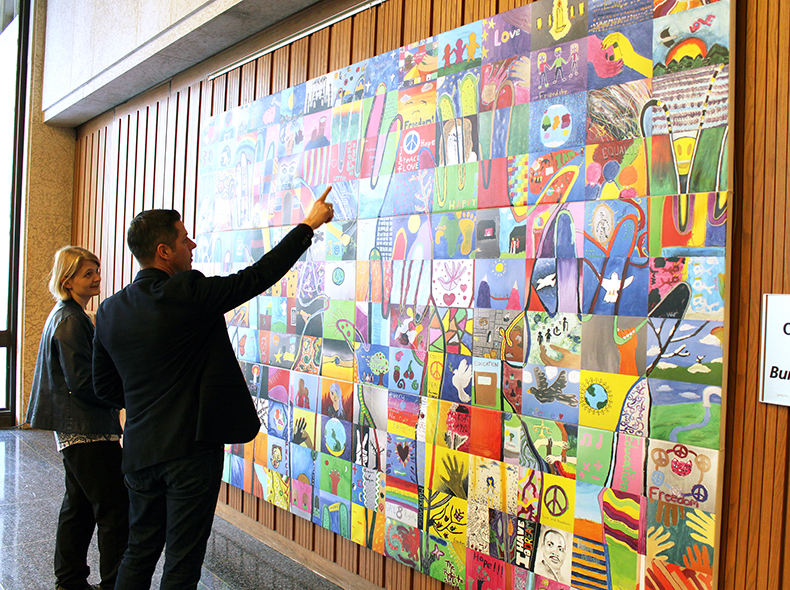 Human Right Mural in Council building near office of the with Mayor Bowmen pointing to one of the images