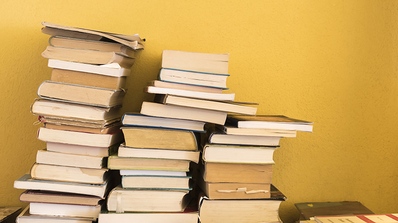 Three stacks of old books along a yellow wall.