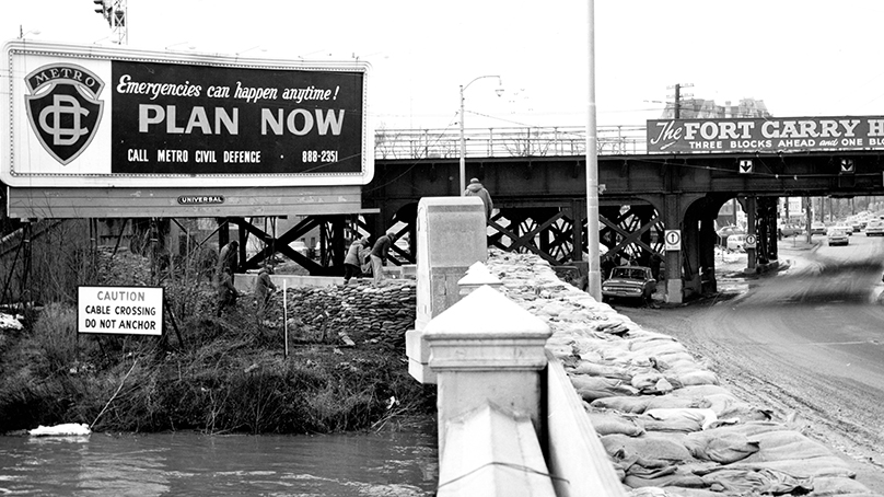 Metro Civil Defence billboard and sandbags at Norwood bridge, 1966.