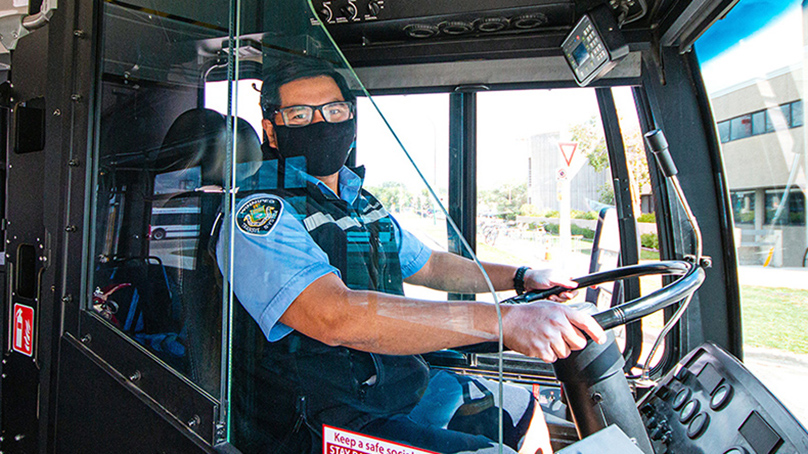 Bus driver wearing a mask sitting behind the stearing wheel.