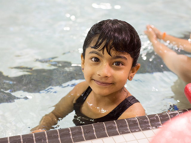 Young child in a swimming pool standing next to the edge.