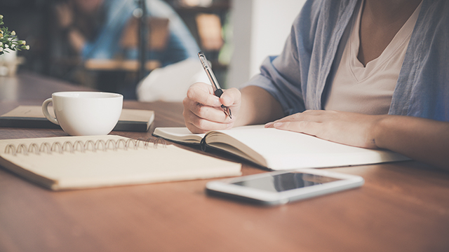 Person writing notes in a book sitting at a desk