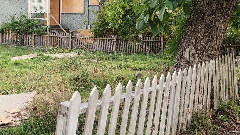 Home with boarded windows and an incomplete aged fence