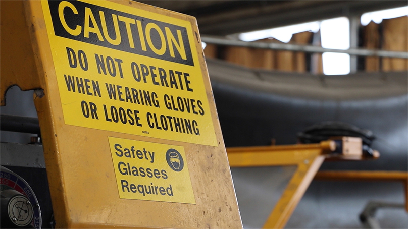 Caution sign reminding employees they need safety glasses and non-loose clothing to operate a machine.