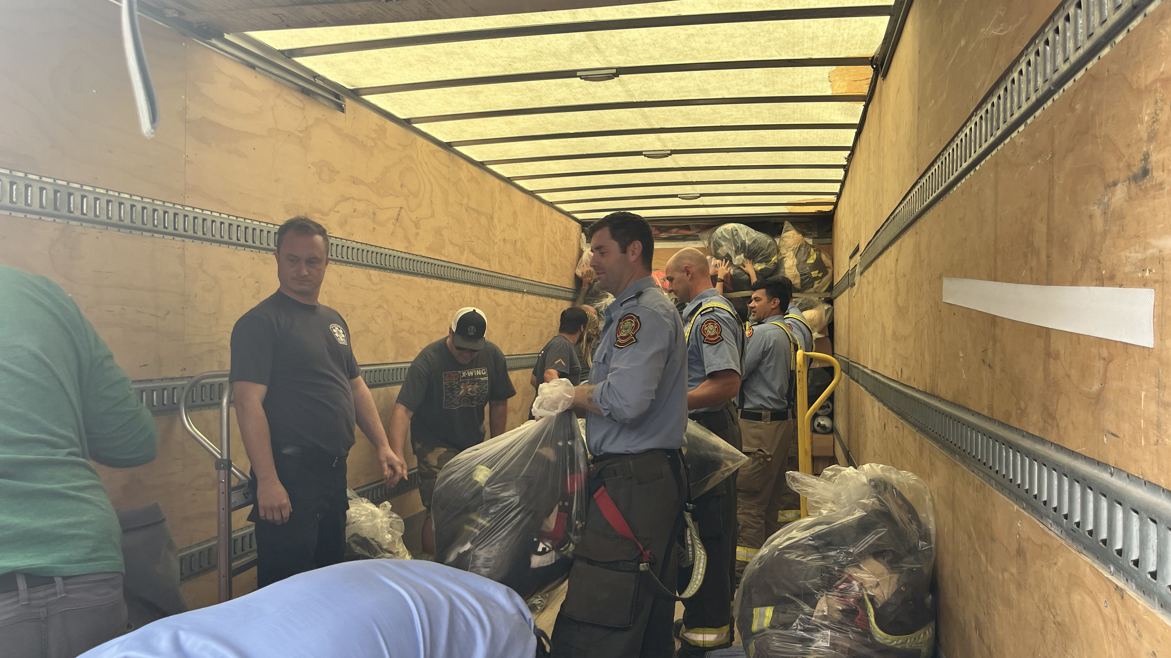 A group of people, including firefighters, pack equipment into a truck.