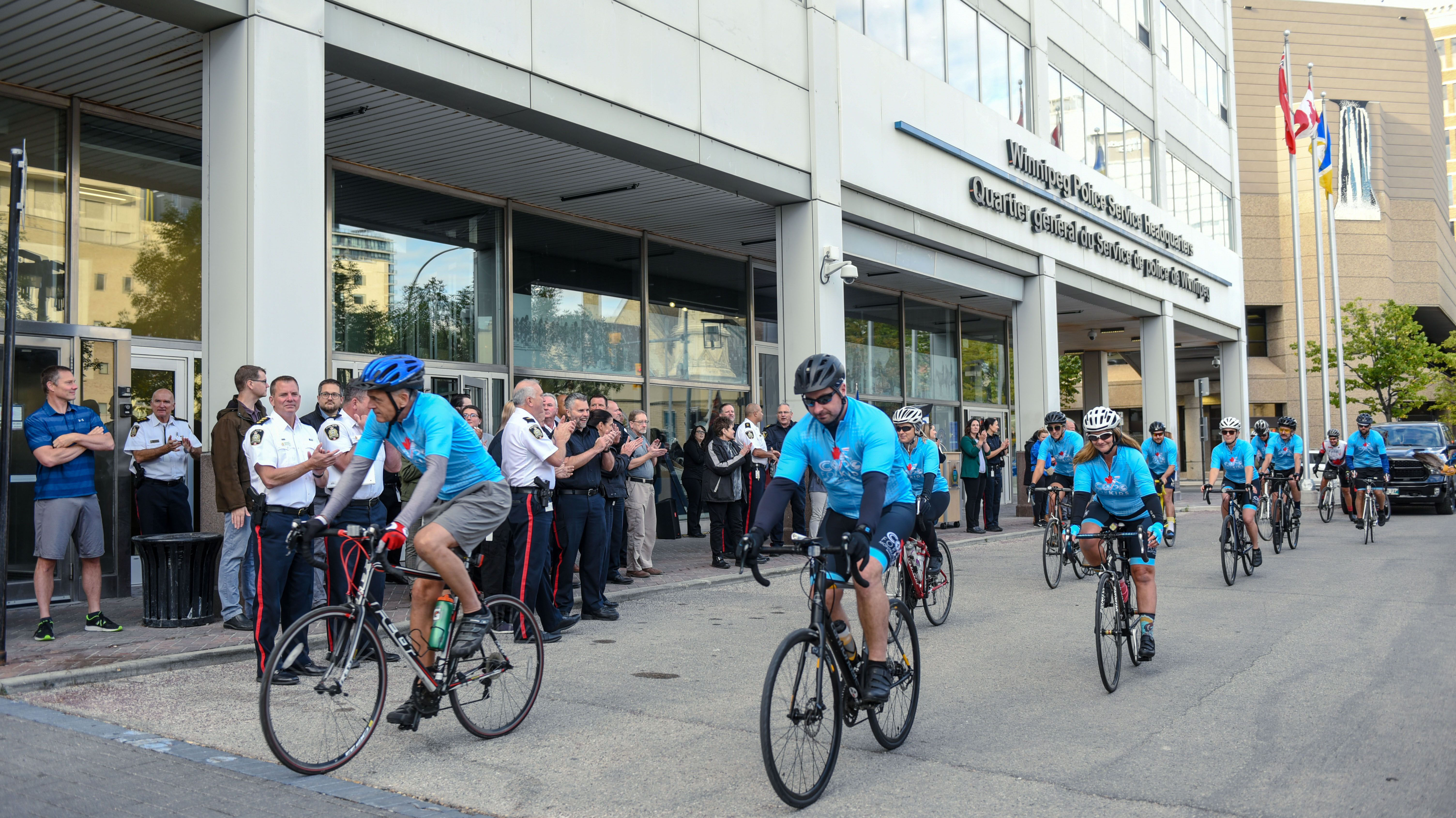 A team of people on bicycles wearing blue shirts cycle past a group of police officers.