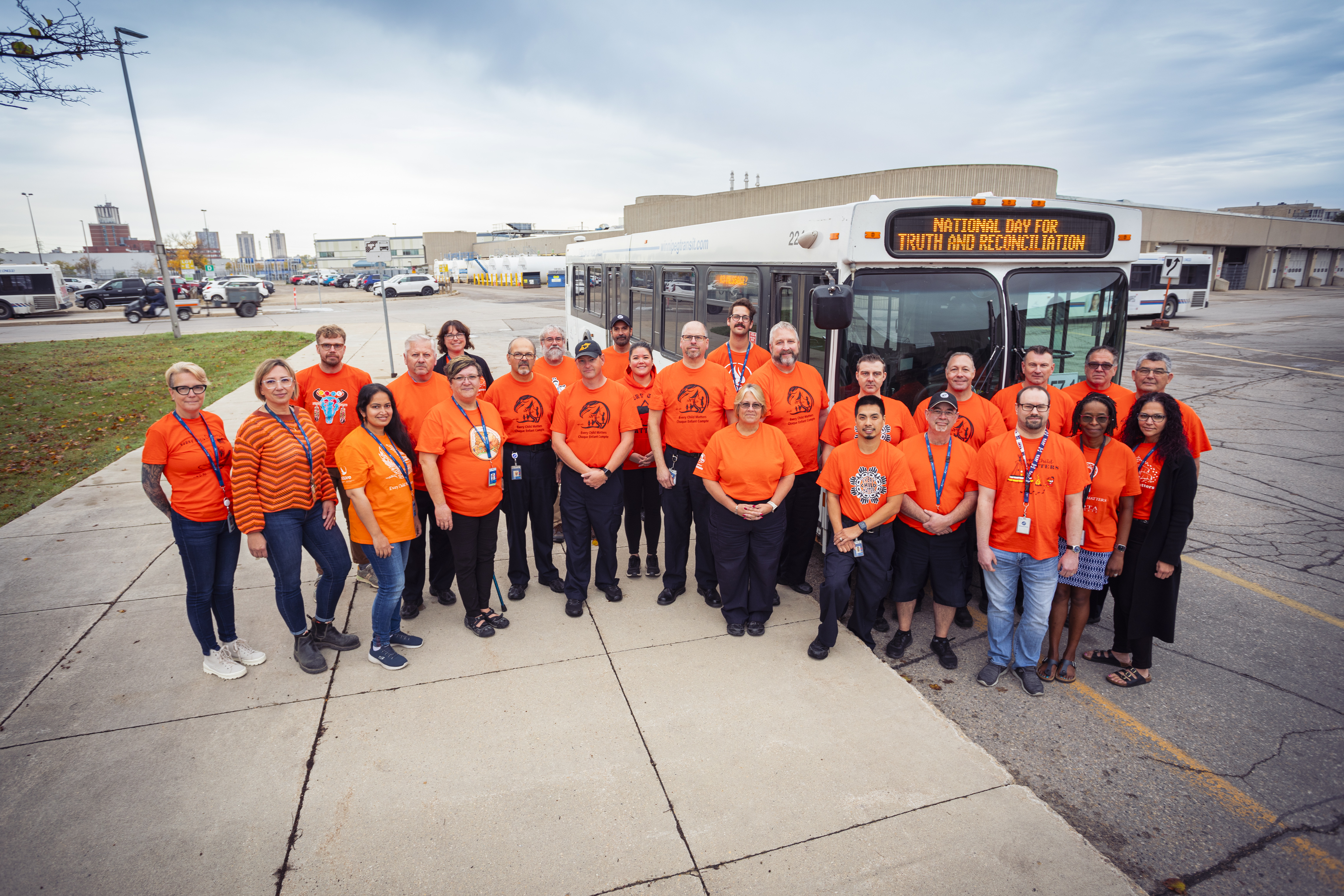 Transit staff in orange shirts stand by a Winnipeg Transit bus.
