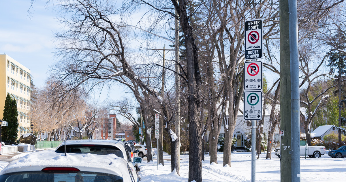 A sign shows a parking area is under a Winter Route Parking Ban.