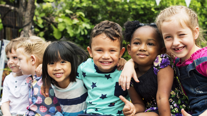 Group of children sitting together smiling, with arms around each other