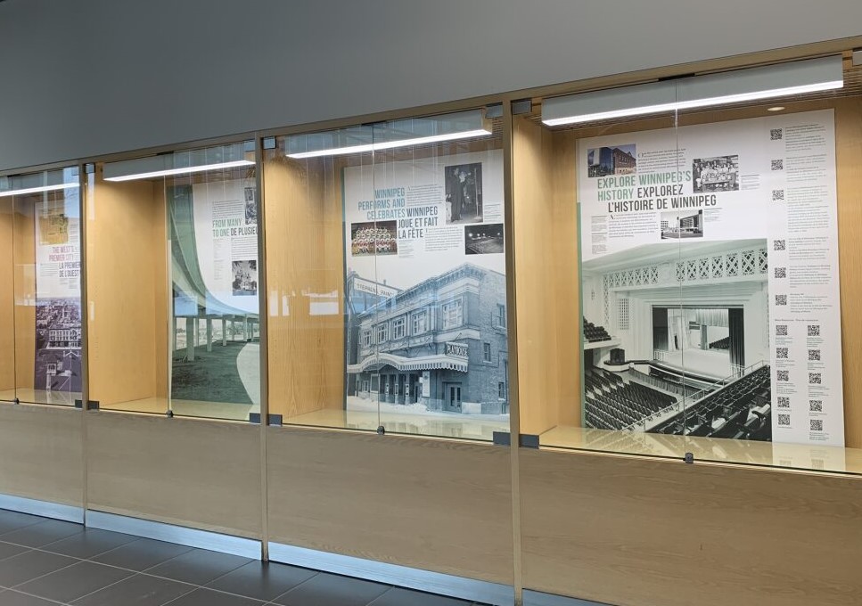 Panels of the Winnipeg 150 History Exhibit are seen behind glass.