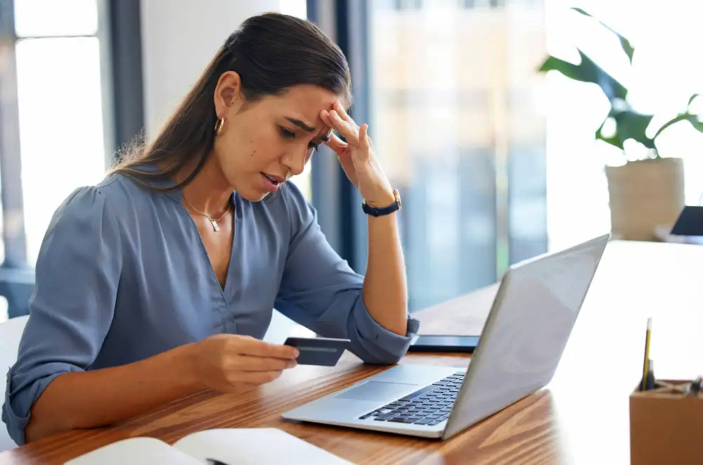 Woman with credit card in hand at computer fretting over transaction.