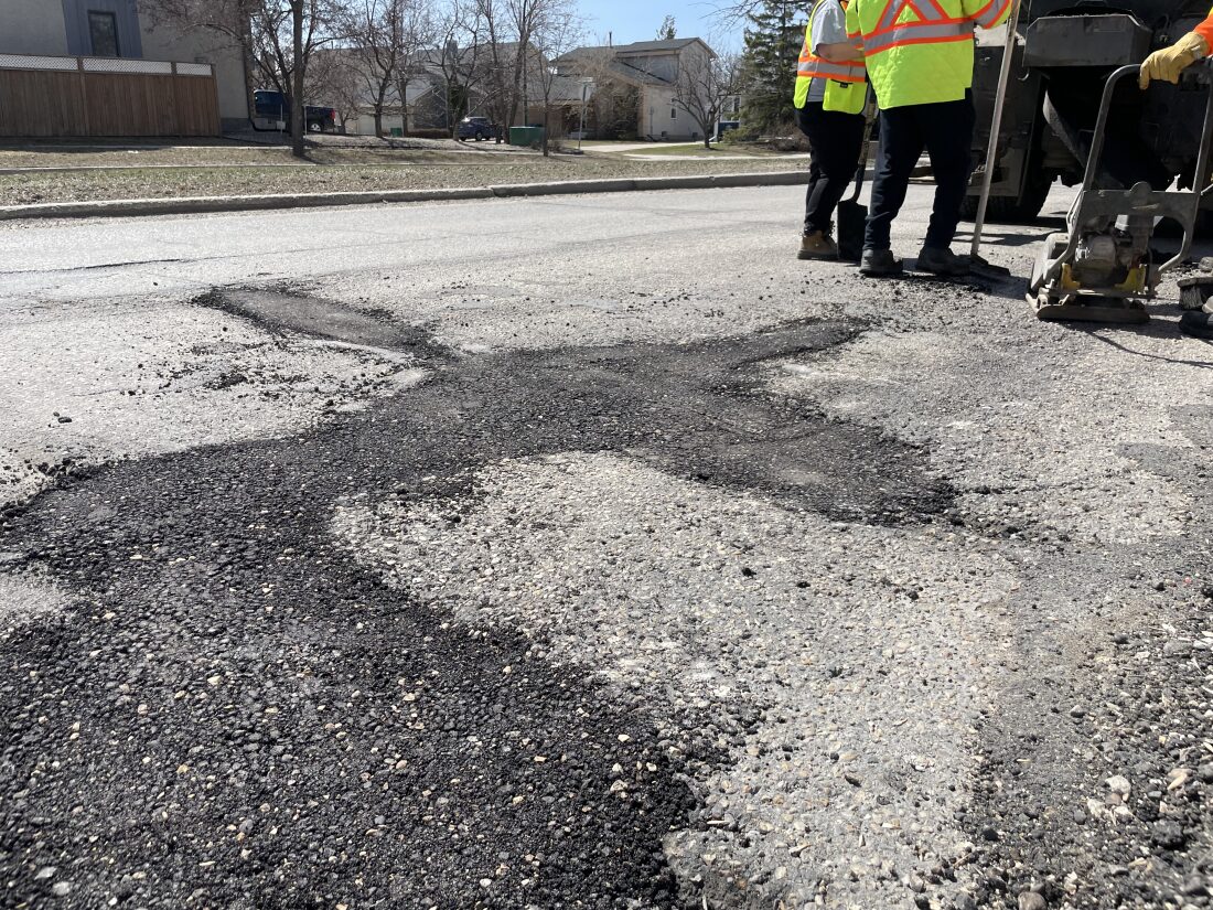 Crews stand near a newly patched pothole.