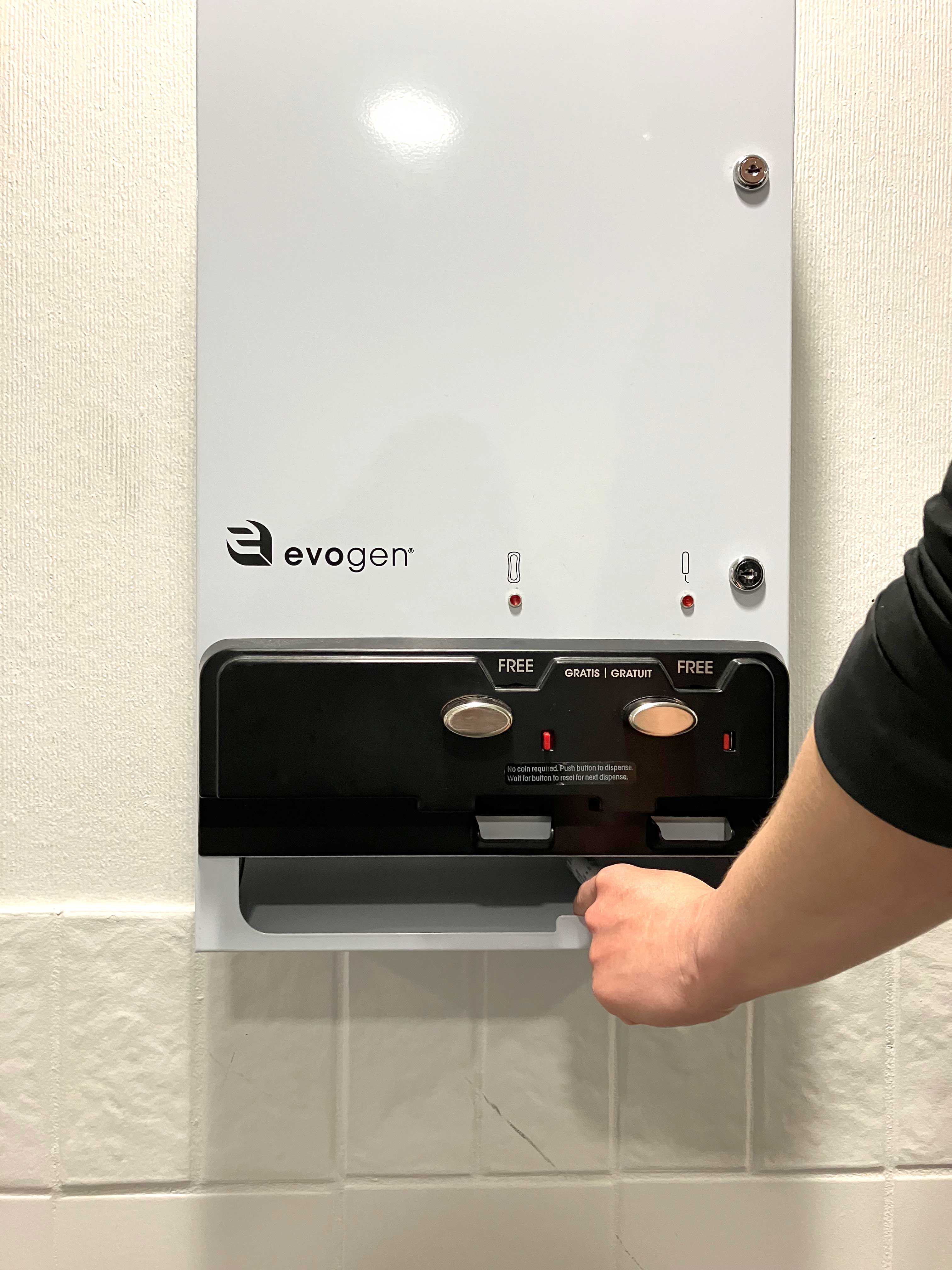 A hand reaches for a tampon from a machine dispensing free menstrual products