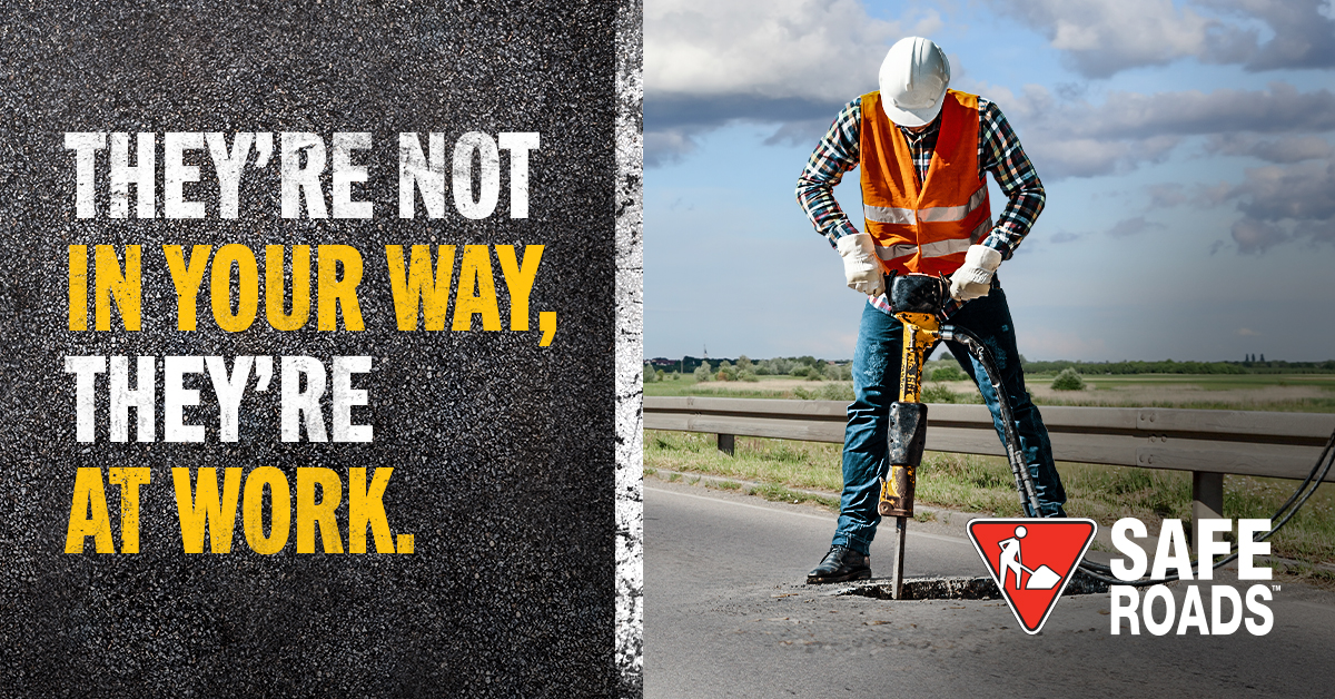 A man in a high visibility vest uses a drill on a road. A message on the left says, "They're not in your way, they're at work."