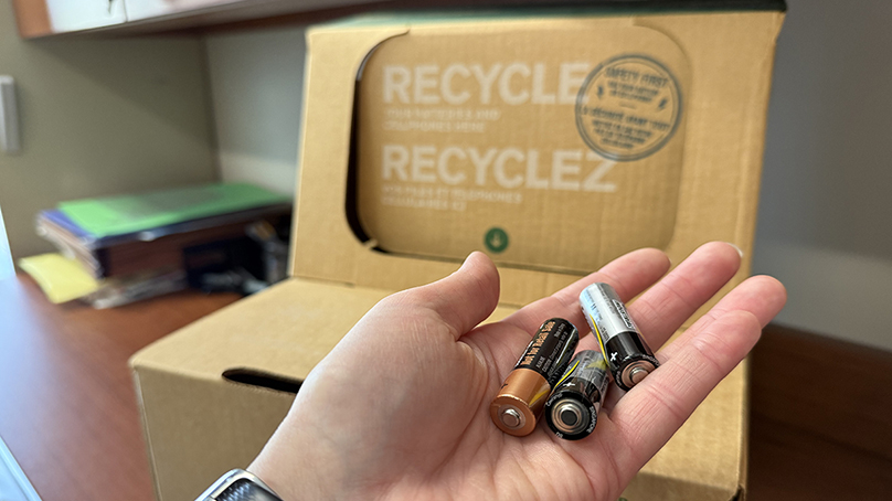 A handful of batteries in front of a battery recycling box.