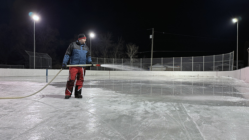A person floods an outdoor rink during winter.