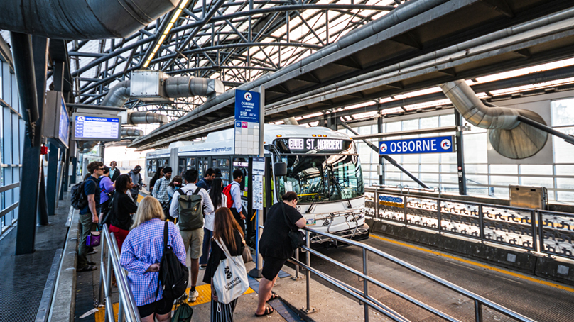 People waiting at an indoor bus stop as a bus approaches