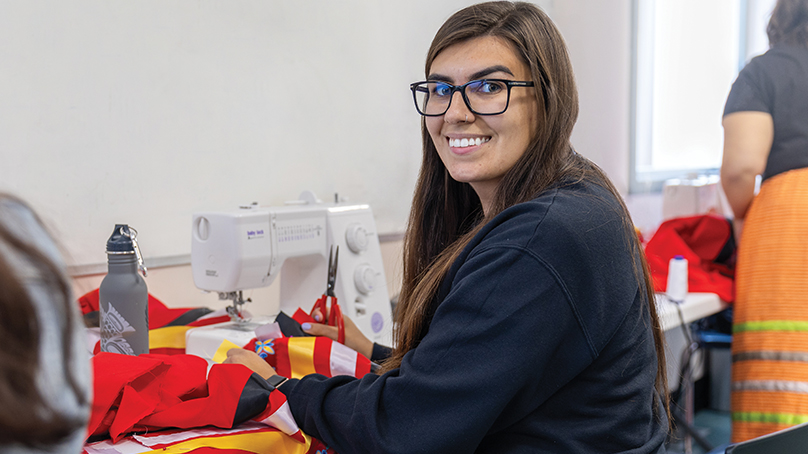 Smiling woman seated at sewing machine with a red ribbon skirt