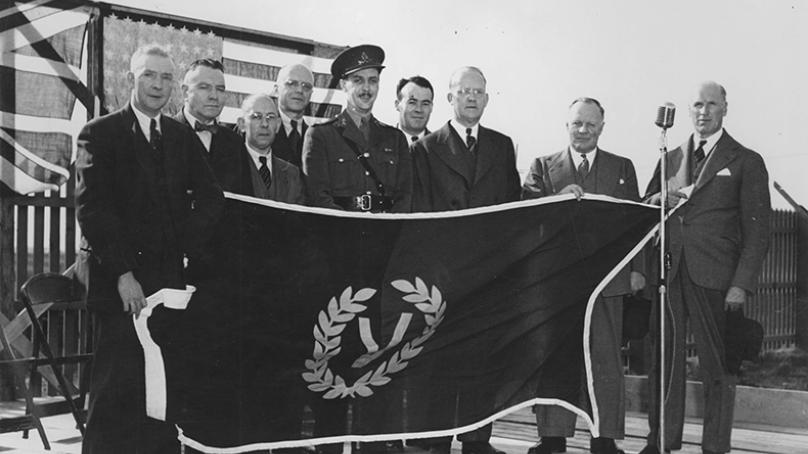 Group of unidentified men and a member of the military holding up a Victory Day flag