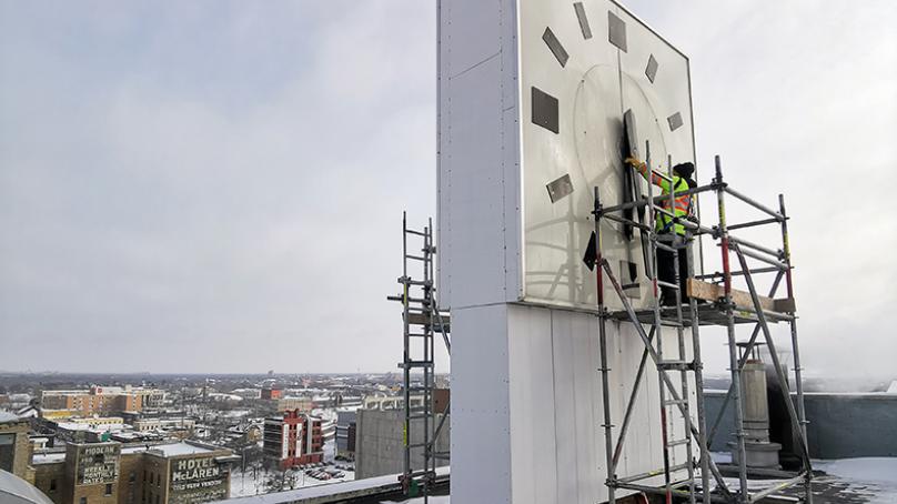 A worker in a safety vest changes the time of the large clock atop Winnipeg's City Hall