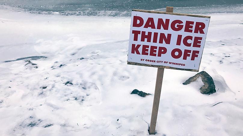 Sign on a frozen water way says Danger Thin Ice Keep Off by order of the City of Winnipeg.