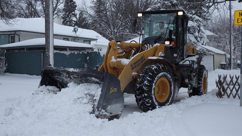 Front end loader with bucket of snow clearing a back lane
