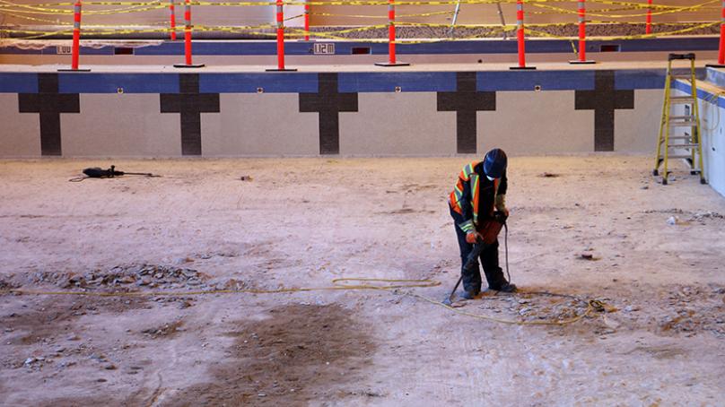 Worker inside empty pool removing tile with tool
