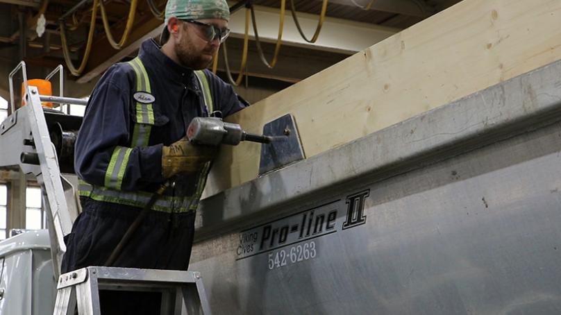 A worker drills into a truck while converting it to be used to spread sand.