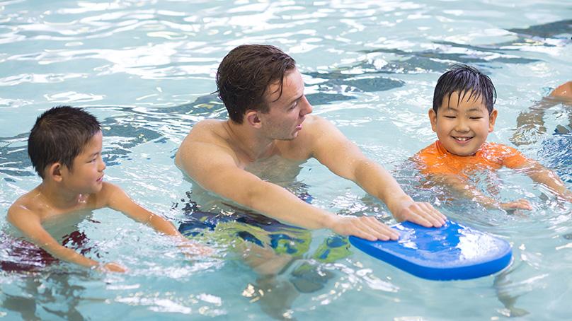 Swimming instructor in the pool showing children how to use an flutter board
