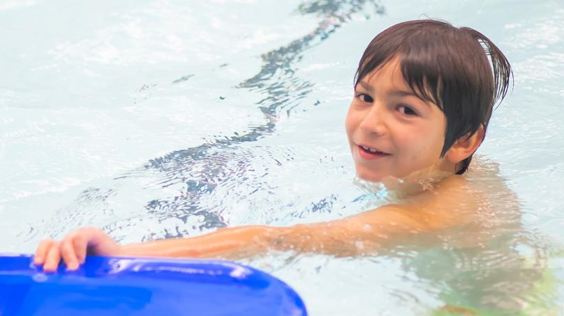 boy swimming in a pool using a blue flutterboard