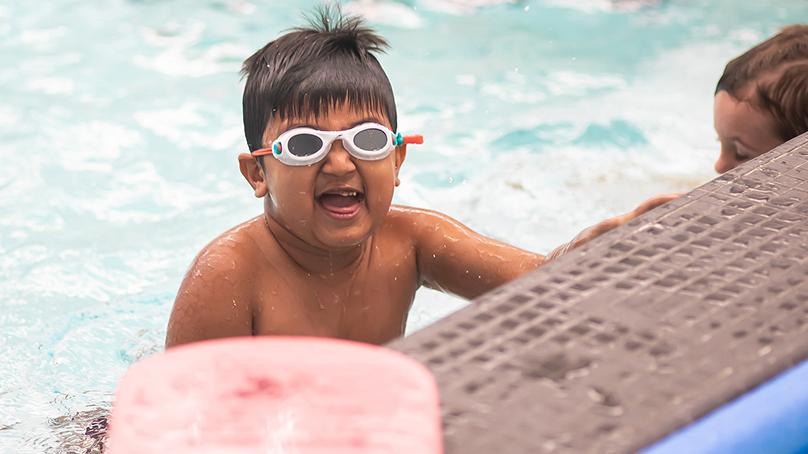 Boy wearing white goggles in a pool near the edge with another child next to him