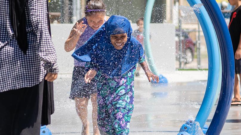 Two girls running through a spray pad in summer