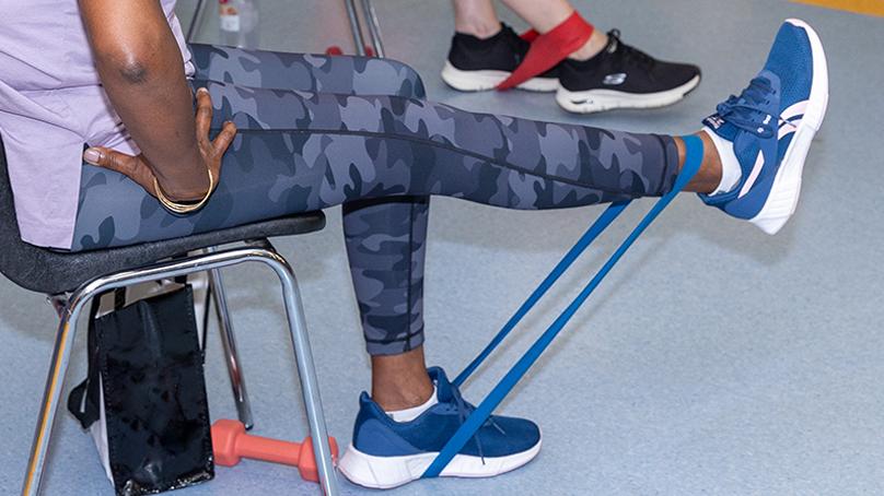 woman sitting in a chair exercising right leg with a resistance band