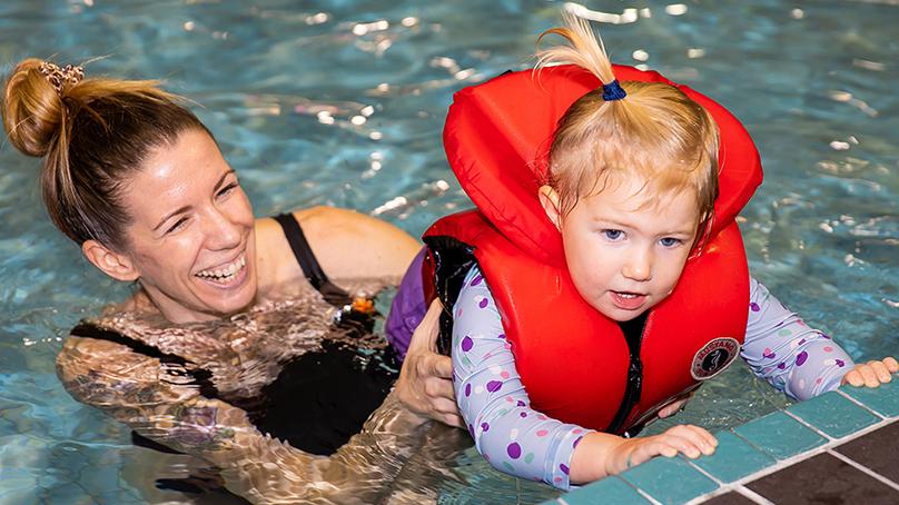 Mother and preschool child with lifejacket on in pool for swim lessons