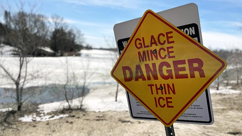 Danger thin ice / glace mince sign at a melting retention pond in spring