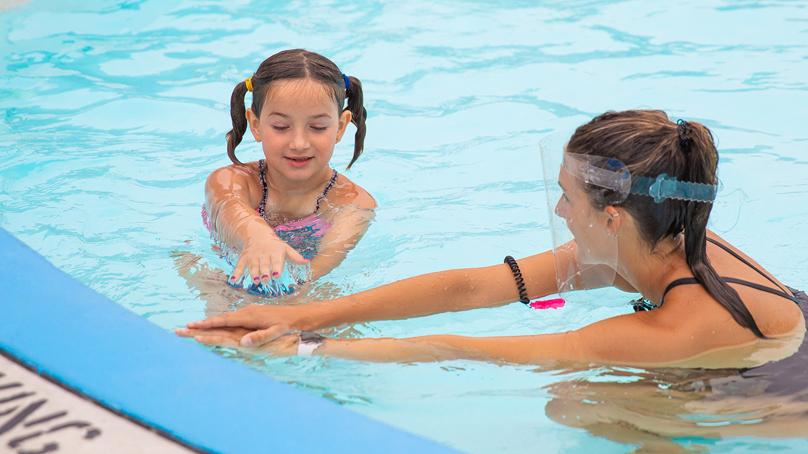 Girl and swim instructor at swim lesson in outdoor pool
