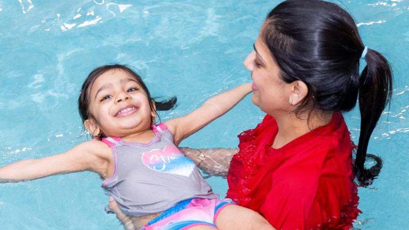 Girl doing back float being held by her mom and smiling 