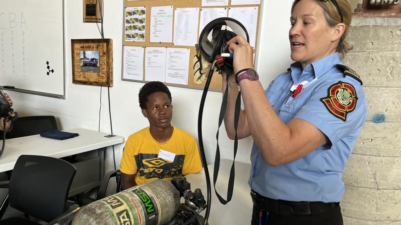 A young person watches a firefighter demonstrate using equipment.
