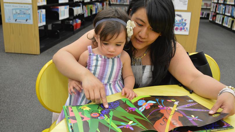 A woman reads a children's book to a little girl.