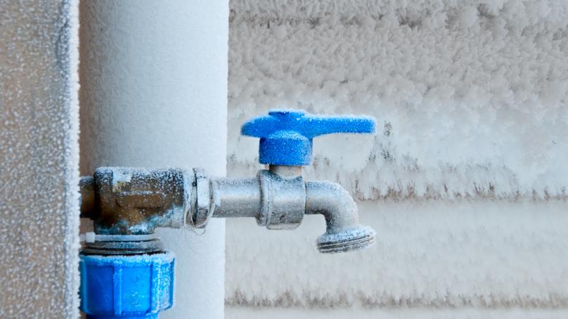 A frozen faucet is seen on the outside of a house.