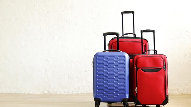 One blue suitcase and two red suitcases stand in a room.