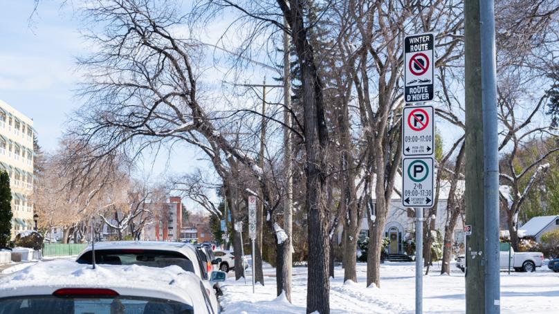A sign shows a parking area is under a Winter Route Parking Ban.