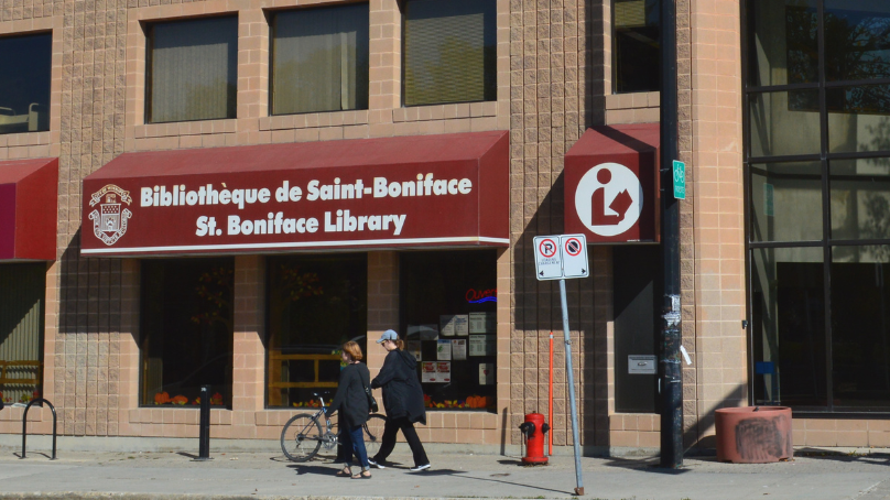 exterior of St. Boniface Library with sign saying the library name and pedestrians walking